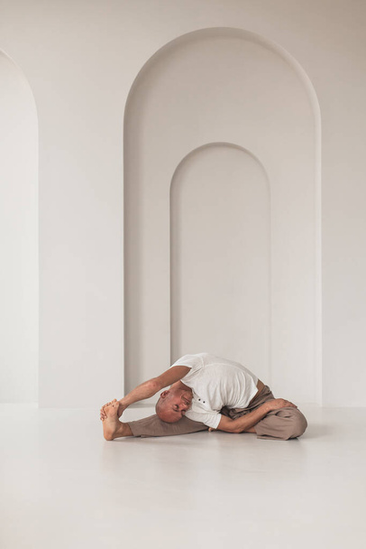An athletic bald Russian male practicing yoga in a white studio. Healthy lifestyle concept. - Foto, afbeelding
