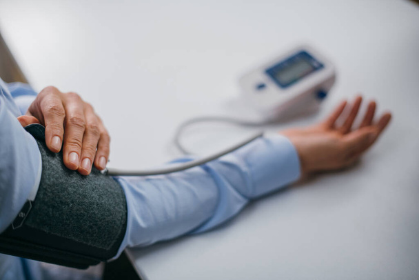 Eller masanın üzerinde bir tonometre ile. Gömlekli bir kadın elektronik tonometreyle kan basıncını ölçer. - Fotoğraf, Görsel