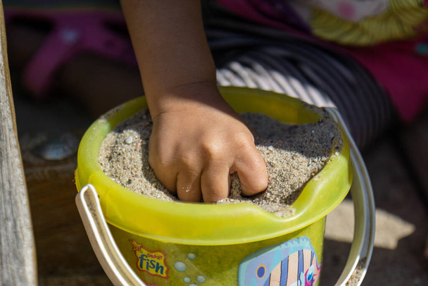 A child's hand grasping a fistful of sand from a bucket on a sunny day at the beach - Фото, зображення