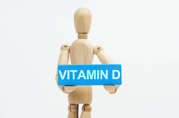 Medicine and healthcare concept. A figurine of a man holds in his hands a blue wooden block with the inscription VITAMIN D. The figurine is out of focus. - Φωτογραφία, εικόνα