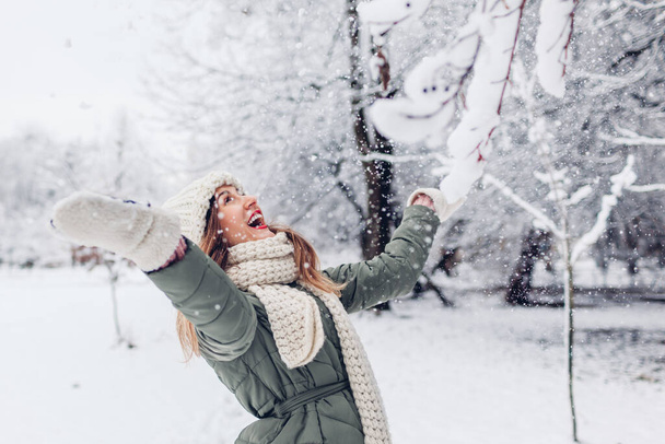 Gelukkige jonge vrouw spelen met sneeuw gooien in besneeuwde winterpark dragen warme gebreide kleding en plezier buiten. Seizoensactiviteiten - Foto, afbeelding