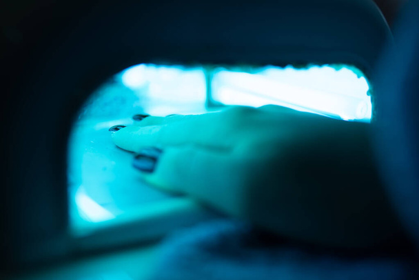 A closeup shot of a client's hands drying the gel manicure in the led light equipment - Photo, Image