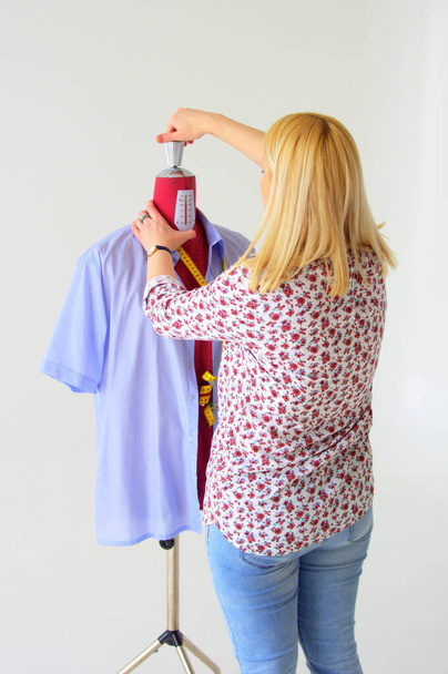 A vertical of a female tailor adjusting the mannequin with a blue shirt - Foto, Imagen