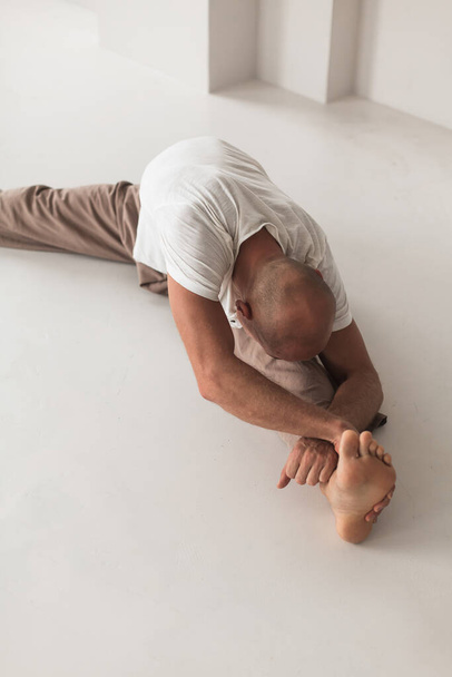 An athletic bald Russian male practicing yoga in a white studio. Healthy lifestyle concept. - Foto, immagini