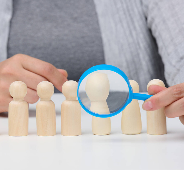 figurines of men on a white table, a female hand holds a magnifying glass over one. concept of searching for employees in the company, recruiting personnel, identifying talented and strong personaliti - Photo, Image