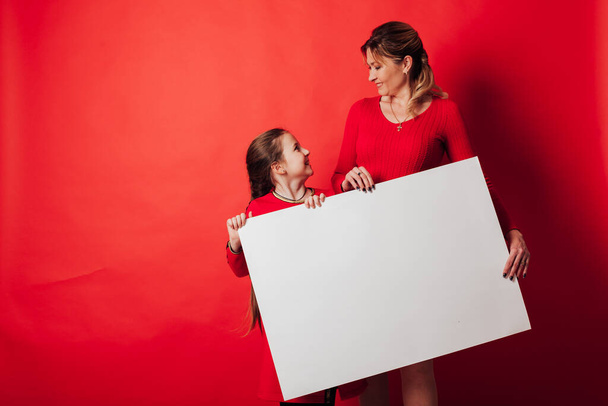 ein Mädchen und eine Mutter mit einem Schild für eine Inschrift auf rotem Hintergrund - Foto, Bild