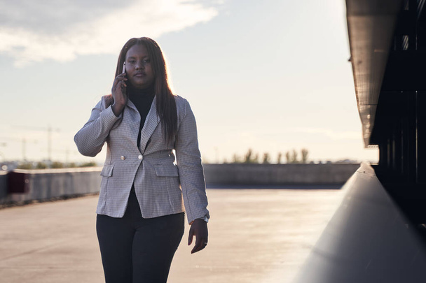 üzletasszony beszél okostelefonon. Afrikai amerikai nő fehér kockás ruhában. - Fotó, kép