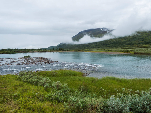 Голубые ледниковые пороги реки Арасьяка с камнями и камнями в Лапландии ландшафт с зелеными горами и березами на Padjelantaleden пешеходной тропе, дикая природа северной Швеции. Летний облачный день - Фото, изображение