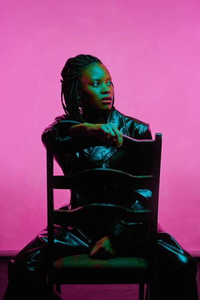 african american girl in neon light sits on chair. pink background - Valokuva, kuva
