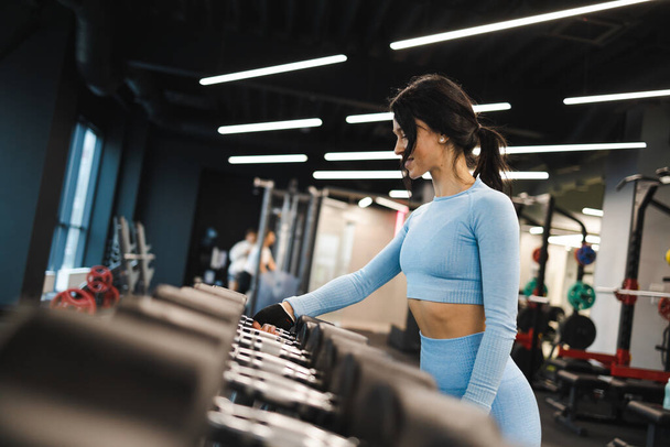 Mujer de fitness en ropa deportiva azul toma pesas del estante - Foto, imagen