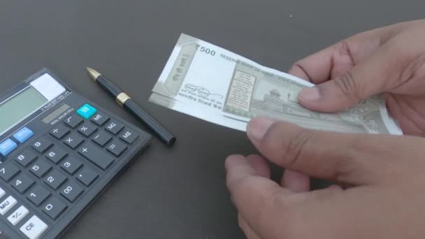 Рука людини підраховує нову 500 рупій індійської валюти проти калькулятора і ручку, розміщену на столі. Високий кут огляду. Близько. банківського бізнесу фінансів
. - Кадри, відео