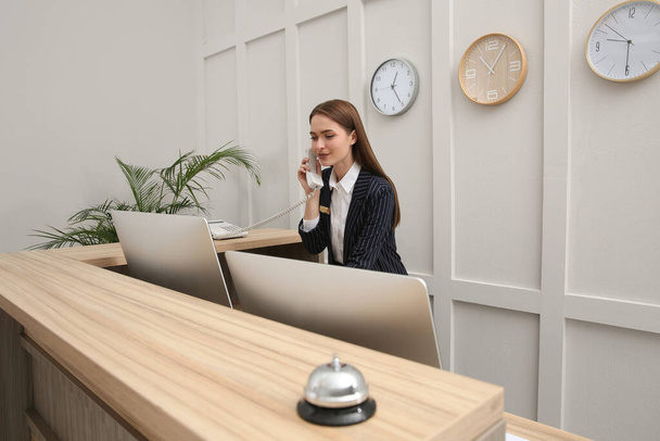 Beautiful receptionist talking on phone at counter in hotel - Photo, image