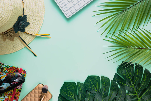 Platte creatieve frame van tropische natuur, palm en Monstera bladeren op een pistchio achtergrond met laptop, vrouwelijke hoed, notebook, zonnebril, digitale nomade en life balance concepten. - Foto, afbeelding