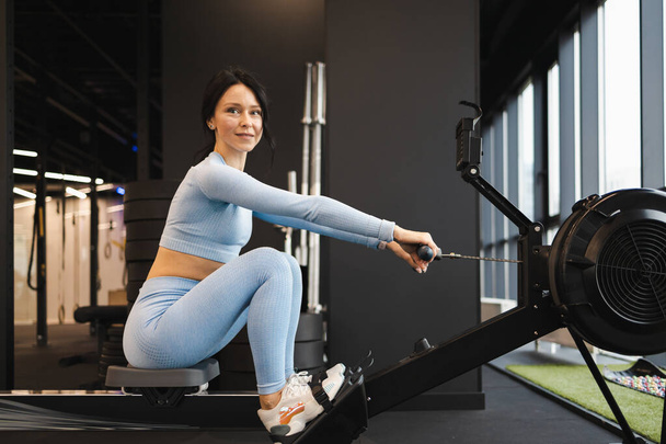 Vue latérale de la femme sportive faisant de l'exercice sur la machine à ramer - Photo, image
