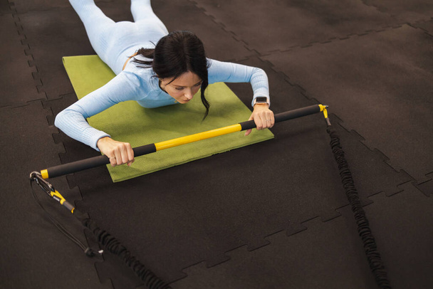 Fitness vrouw ligt op de sportvloer en doet oefeningen met trx rip trainer - Foto, afbeelding