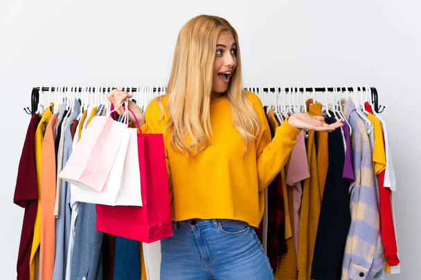 Joven mujer rubia uruguaya en una tienda de ropa y sosteniendo bolsas de compras con expresión facial sorpresa - Foto, imagen