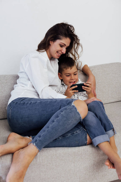 madre e hijo jugando teléfono inteligente gadget en el sofá - Foto, imagen