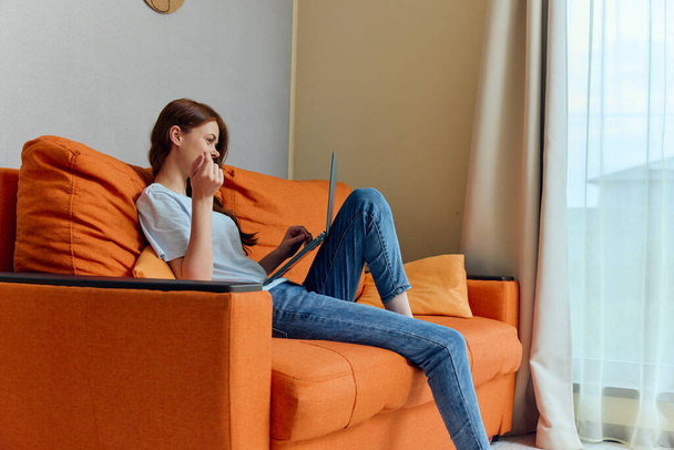 陽気な女性がオレンジのソファでノートパソコンの技術でおしゃべりし - 写真・画像