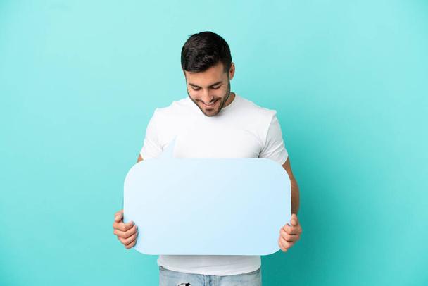 Young handsome caucasian man isolated on blue background holding an empty speech bubble - Foto, Bild