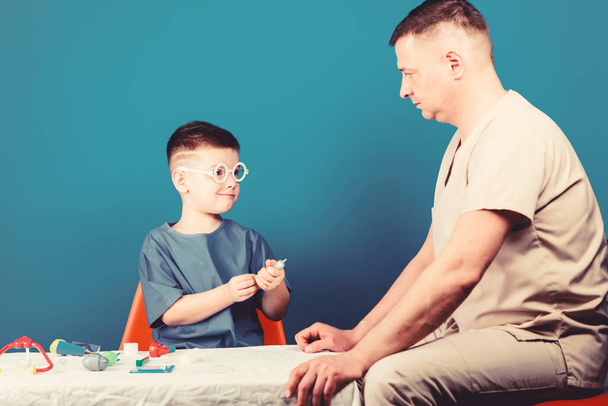 Medical examination. Boy cute child and his father doctor. Hospital worker. Medicine concept. Kid little doctor sit table medical tools. Illness treatment. Dad and son medical dynasty. Health care - Foto, Imagen