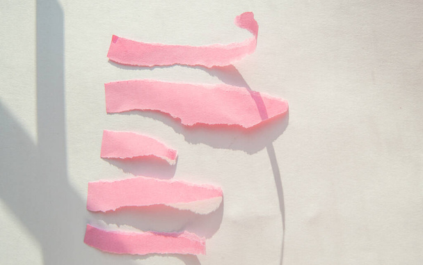 Abstract roze gescheurde papieren stroken op een witte achtergrond met een schaduw van zonlicht. - Foto, afbeelding