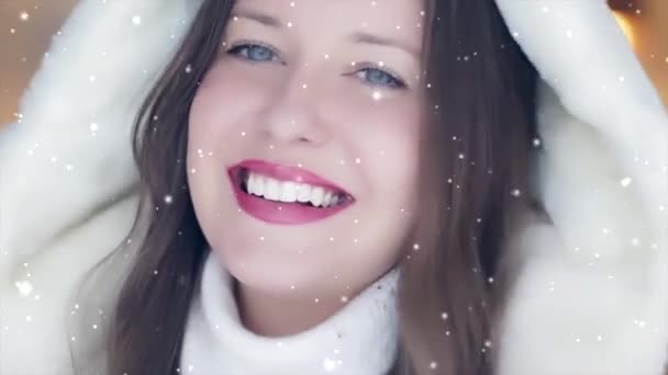 Winter mode en kerstvakantie look. Mooie glimlachende vrouw met witte trui en pluizige capuchon bontjas, sneeuw en sneeuwvlokken - Video