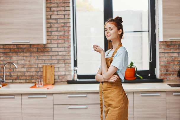 mujer bonita gestos con sus manos en un delantal marrón interior de la cocina Estilo de vida - Foto, imagen