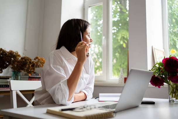 Επιχειρηματίας που εργάζεται σε φορητό υπολογιστή κάθεται στο σπίτι και τη διαχείριση της επιχείρησής της μέσω του γραφείου στο σπίτι - Φωτογραφία, εικόνα