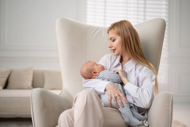 Mamá sostiene al bebé en sus brazos y se sienta en una silla. - Foto, Imagen