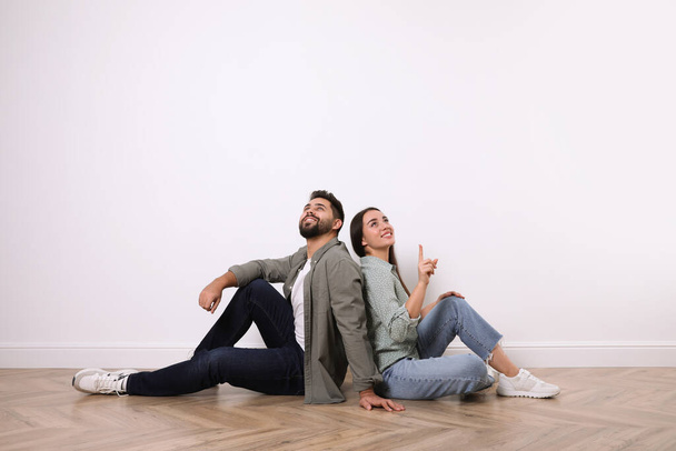 Young couple sitting on floor near white wall indoors - Foto, imagen