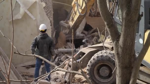 保護ヘルメットを持つエンジニアは、解体、古い建物の破壊を見て、掘削機はヴィンテージハウスを破壊します。生きている物体の破壊。都市再生4k高品質スローモーションビデオ - 映像、動画
