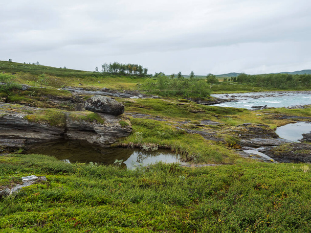 Blue glaciale Arasjahka fiume rapide con massi e pietre in Lapponia paesaggio con montagne verdi e betulle a Padjelantaleden sentiero escursionistico, nord della Svezia natura selvaggia. Estate giornata nuvolosa - Foto, immagini
