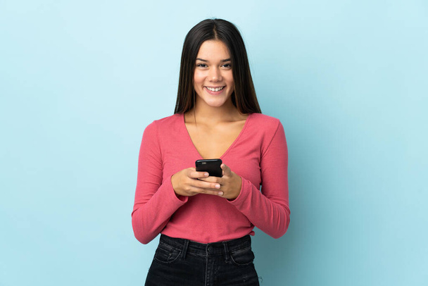 Teenager girl isolated on blue background sending a message with the mobile - Photo, Image