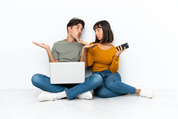 Молода пара з ноутбуком і мобільним, сидячи на підлозі, робить неважливий жест під час підйому плечей
 - Фото, зображення