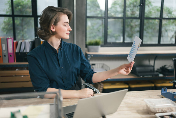 Beautiful businesswoman holding paperwork with laptop computer in office - Valokuva, kuva