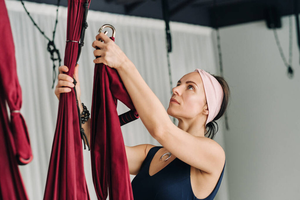 A woman fastens a hook from a hanging hammock for yoga in the gym. - Foto, immagini