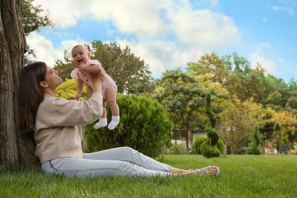 Happy mother with adorable baby sitting on green grass in park - Zdjęcie, obraz