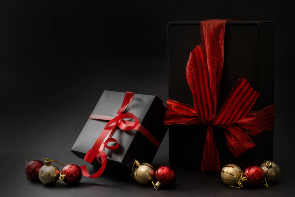 Composition of gifts of different shapes wrapped in black wrapping paper with a red ribbon and a bow on a black background. Side view. Copy space. - Fotografie, Obrázek