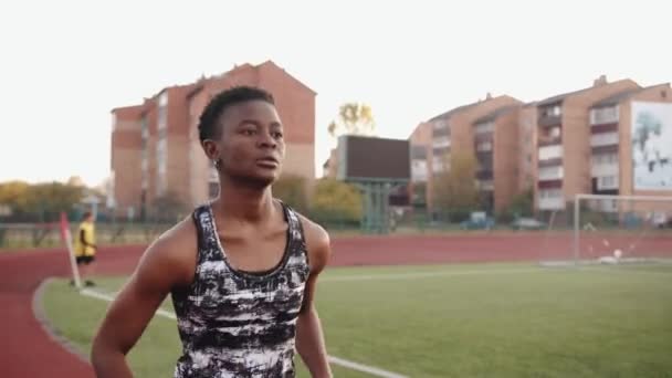 Chica negra seria corriendo en la cinta de correr del estadio de la ciudad durante el entrenamiento para el equipo de fútbol. Movimiento lento - Metraje, vídeo