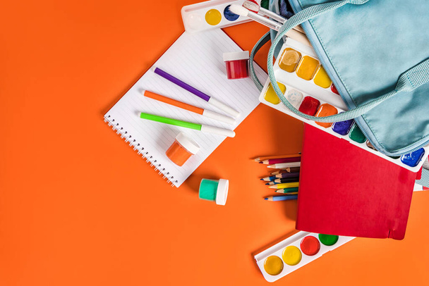 A blue backpack with different colored stationery, paints on an orange background. Banner for a children's art club or school - Foto, Bild