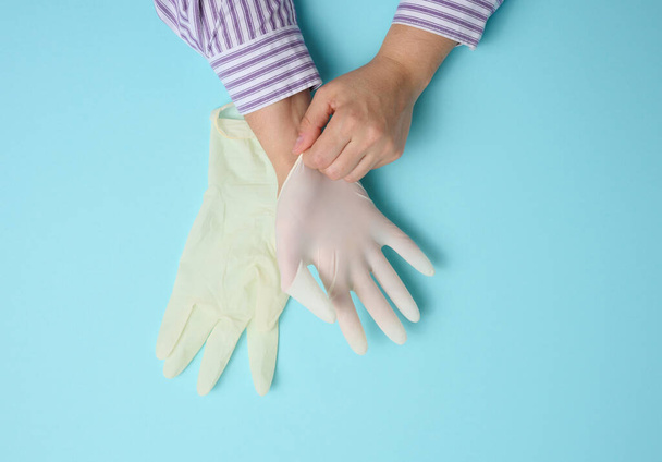 proceso de poner guantes de látex blanco en la mano sobre fondo azul, protector de higiene - Foto, Imagen