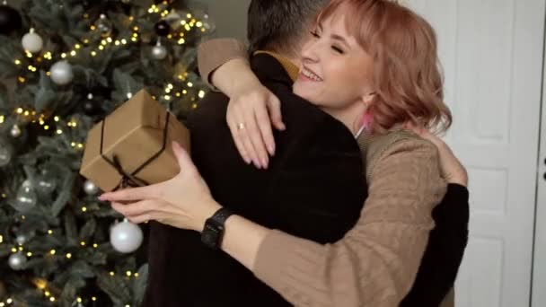 L'uomo dà alla donna una scatola regalo sullo sfondo dell'albero di Natale. Tradizione familiare. - Filmati, video