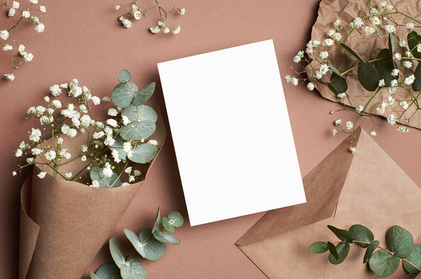 Wedding invitation or greeting card mockup with envelope, eucalyptus and gypsophila flowers on beige paper background - 写真・画像