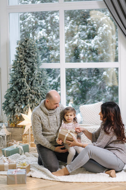 A végzős szülők megölelik az unokáját otthon a fenyőfa közelében. A boldog emberek karácsonyi hangulata - Fotó, kép