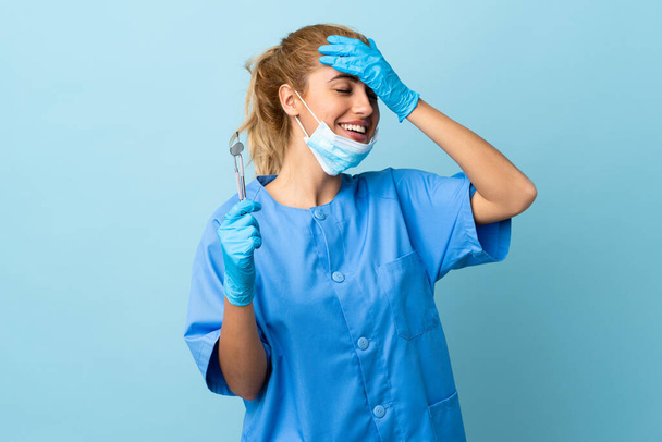 Jovem dentista segurando ferramentas sobre fundo azul isolado rindo - Foto, Imagem