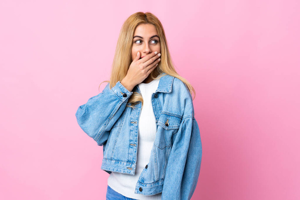 Junge uruguayische blonde Frau auf isoliertem rosa Hintergrund macht Überraschungsgeste, während sie zur Seite schaut - Foto, Bild