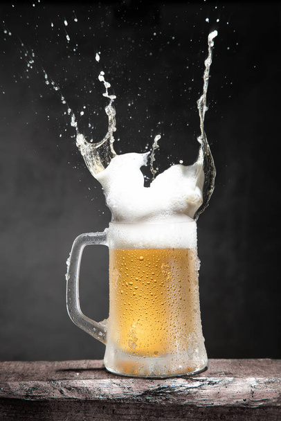 Mug of beer with foam and splashes on wooden table isolated on dark background. Vertical format. - Foto, afbeelding