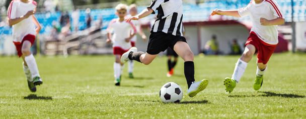 Iskolai focisták futás után labda és rúgás League Match. Egy csapat gyerek focista párbajozik. Focisták sportos Jersey pólóban és pulóverben - Fotó, kép