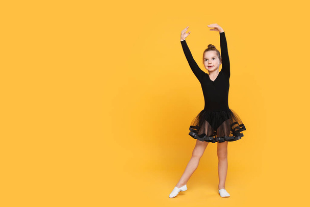 Carino bambina in abito nero ballare su sfondo giallo. Spazio per testo - Foto, immagini