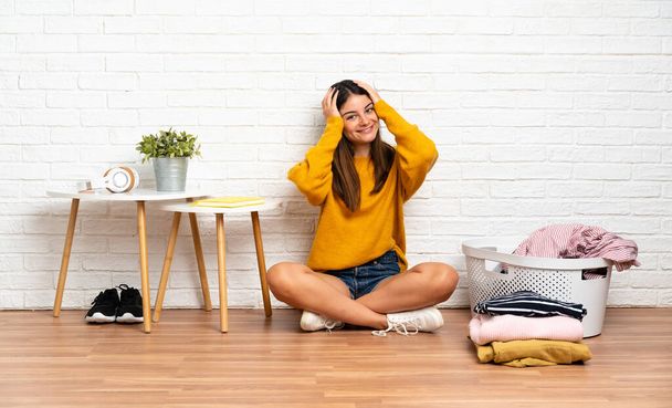 Young woman sitting on the floor at indoors with clothes basket laughing - Photo, Image